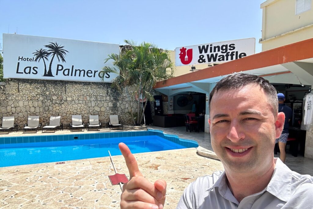 Las Palmeras Hotel and Wings and waffle sign in Sosua, Dominican Republic, selfie with American tourist.